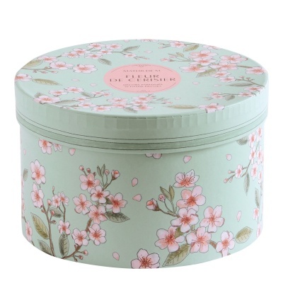 Caixa redonda decorativa verde pastel com flores rosas e texto no topo.