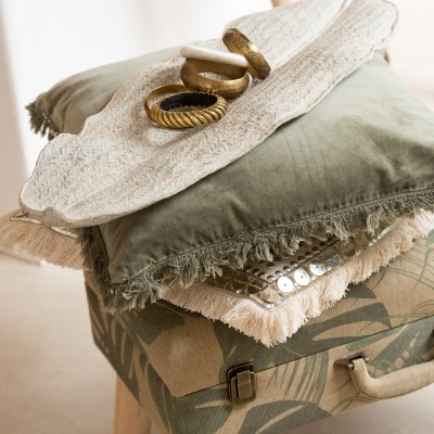 Mala com padrão botânico, almofadas com franjas e pulseiras douradas sobre almofadas