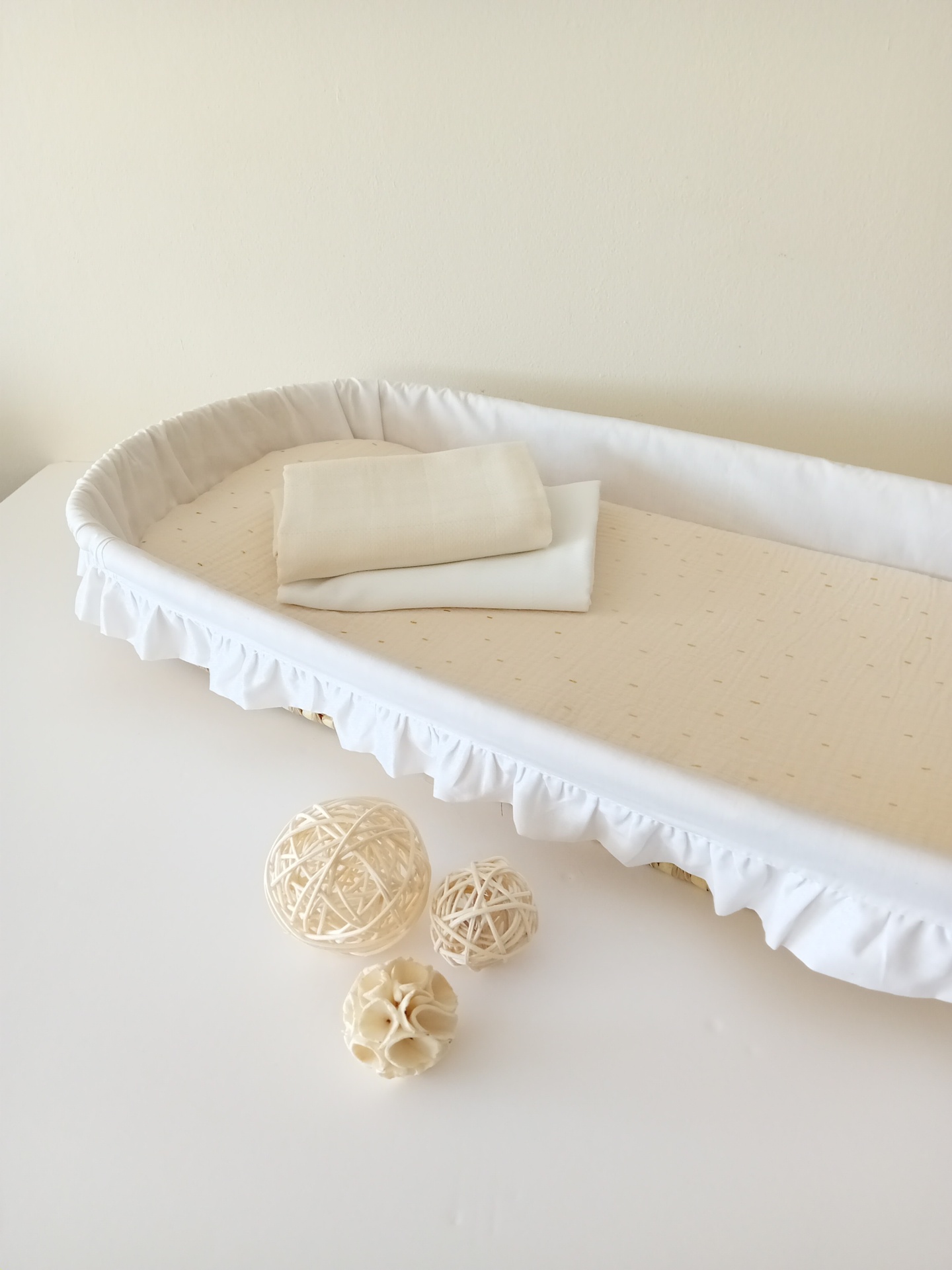 Cama de bebé branca com colchão bege, toalhas brancas e bolas decorativas naturais