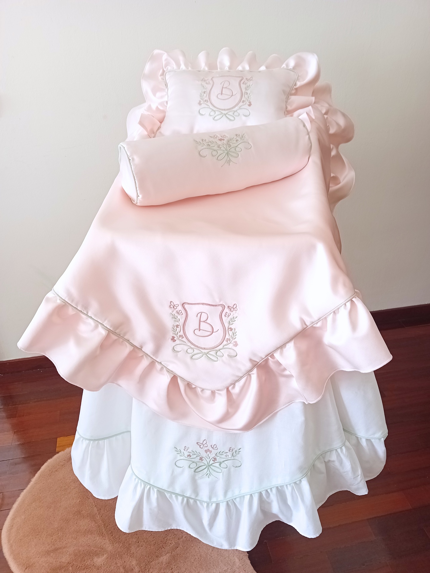 Cobertura de berço rosa claro com babados e bordado com letra B