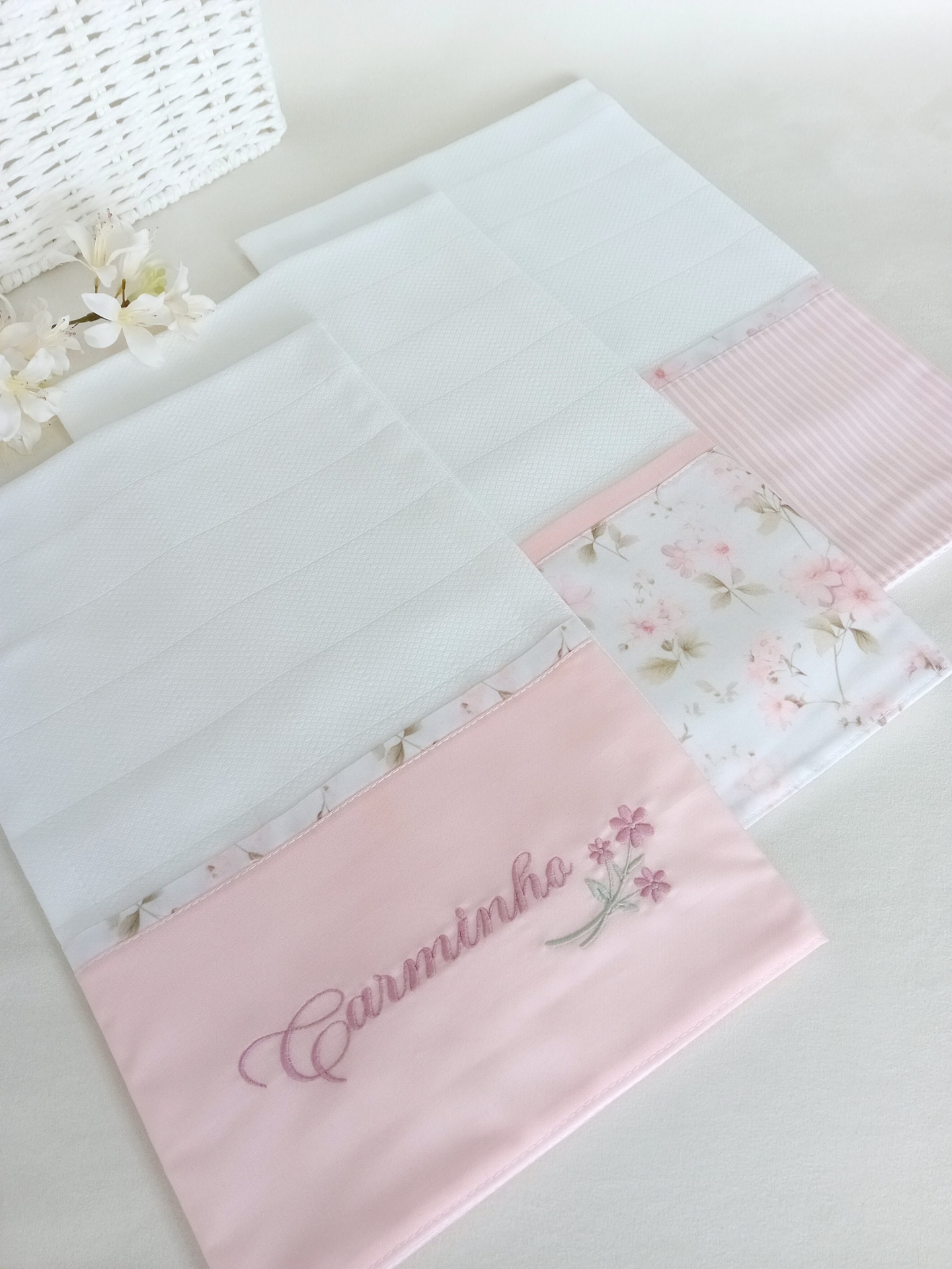 Toalhas brancas com bandas rosa e floral, uma bordada com Carminha e flores