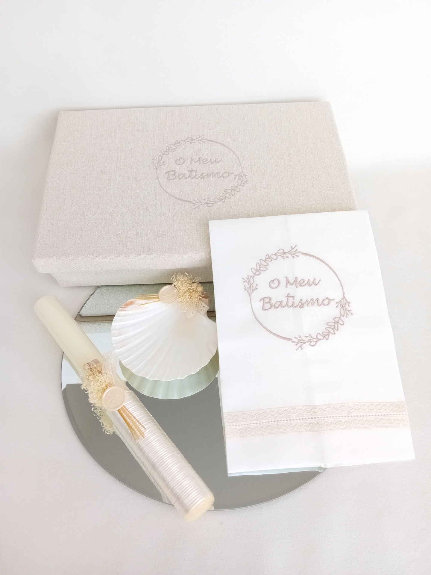 Conjunto de batismo com caixa, toalha bordada e vela decorada sobre um espelho