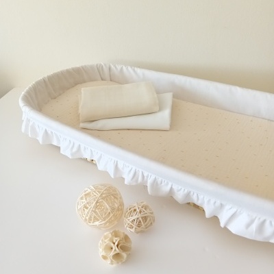 Cama de bebé branca com colchão bege, toalhas brancas e bolas decorativas naturais