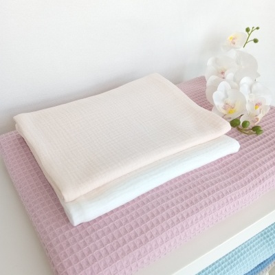 Três toalhas empilhadas em rosa, branco e bege com textura quadriculada, ao lado de uma flor branca