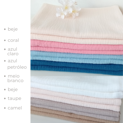 Tecido em várias cores pastel empilhados com flor branca sobre superfície branca