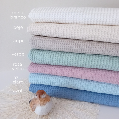 Sete toalhas empilhadas de cores diferentes com textura quadrada e pássaro decorativo em fundo claro