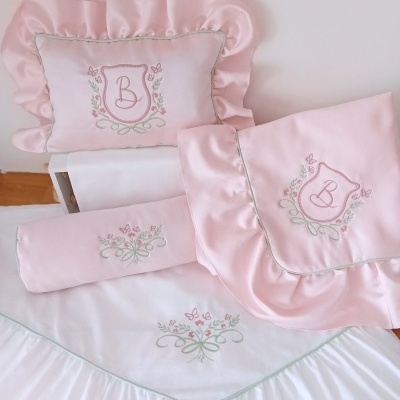 Conjunto de têxteis para bebé rosa e branco com bordados florais e borboletas.