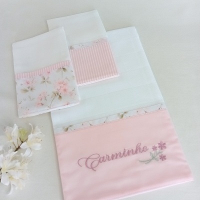 Fraldas de tecido branco com detalhes florais e bordado rosa com o texto Carminho.