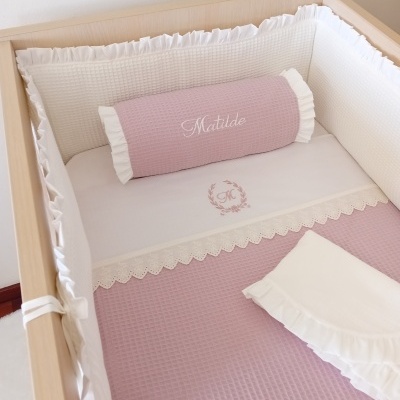 Conjunto de roupa de cama rosa e branca num berço de madeira clara
