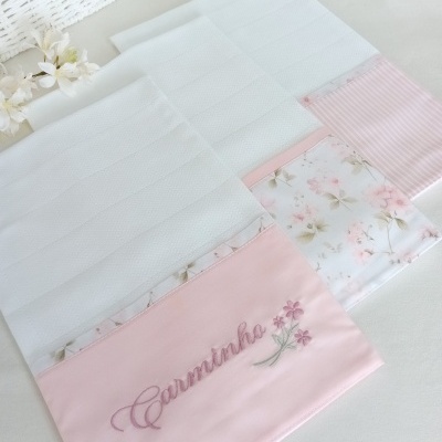 Toalhas brancas com bandas rosa e floral, uma bordada com Carminha e flores