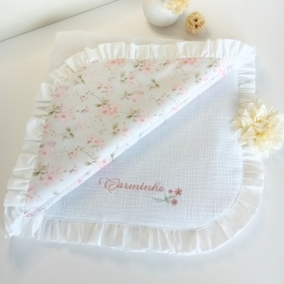 Manta branca com borda de folhos e padrão floral, com o texto bordado Carminho.