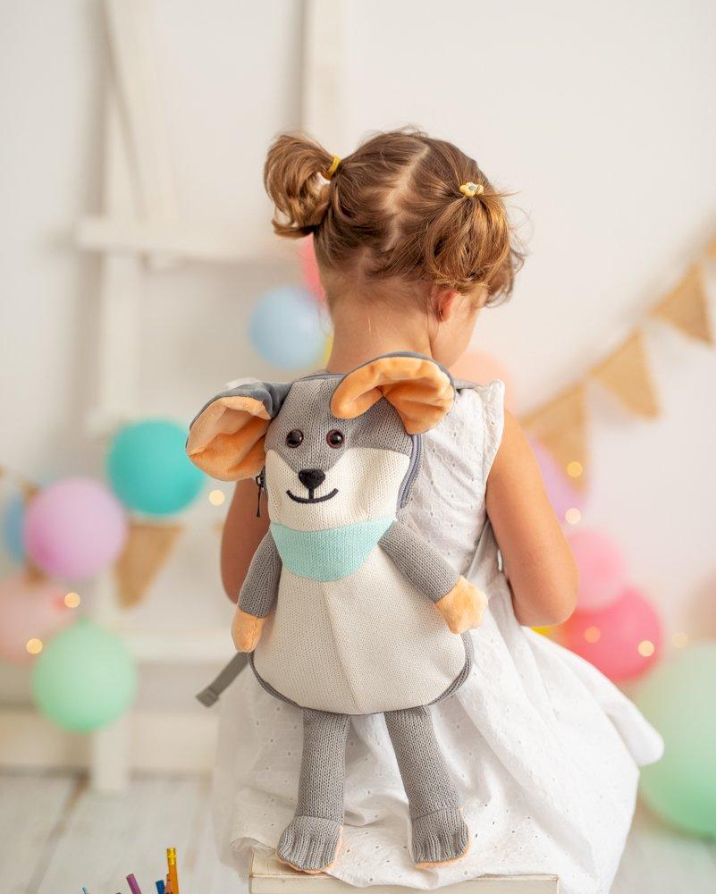 Mochila Ratita Mochila infantil em forma de rato cinzento com orelhas bege e lenço azul, vista de costas em criança com vestido branco