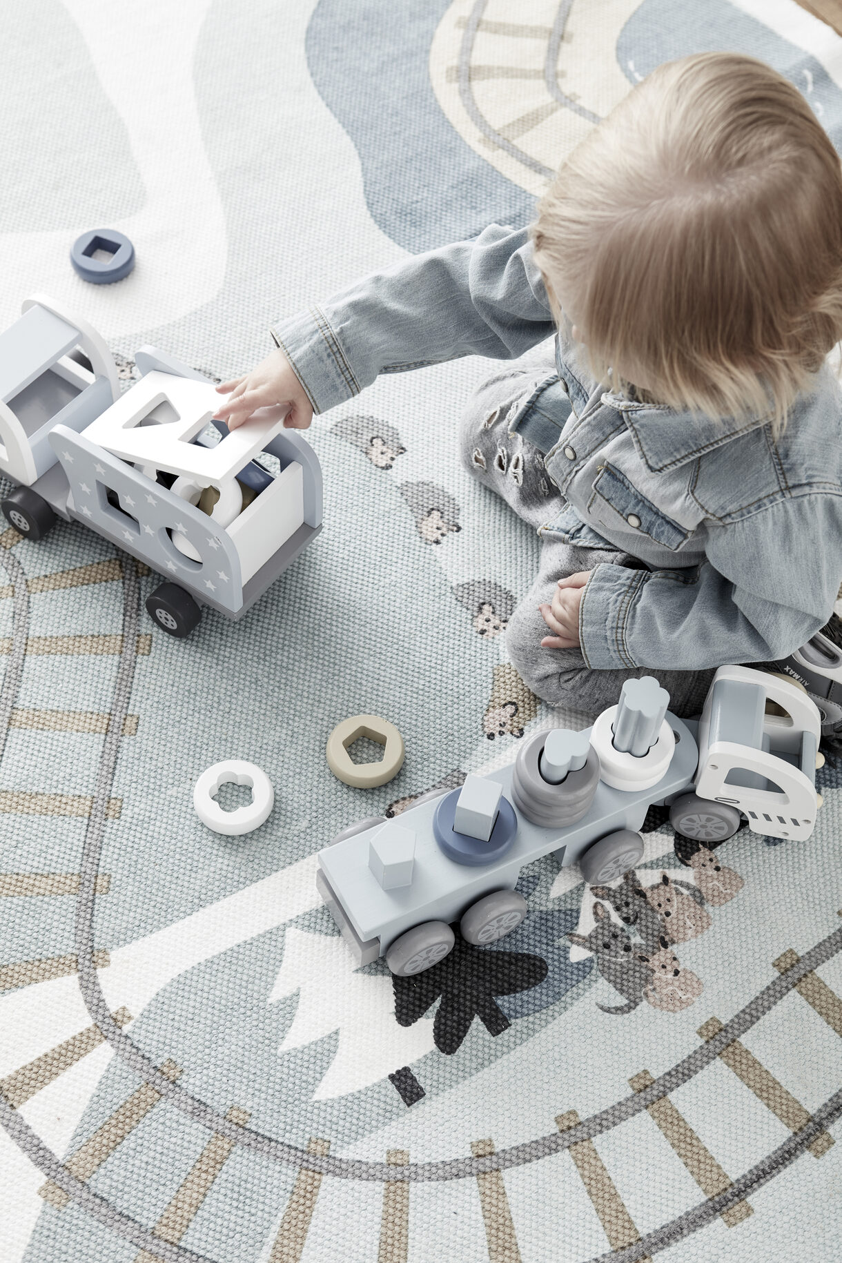 Criança a brincar com brinquedos de madeira com formas geométricas sobre tapete com padrão de caminhos
