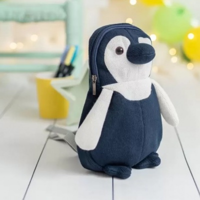 Mochila em formato de pinguim azul escuro e branco sobre chão branco