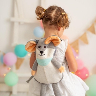 Mochila infantil em forma de rato cinzento com orelhas bege e lenço azul, vista de costas em criança com vestido branco