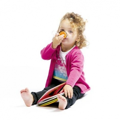 Criança pequena sentada com casaco rosa a segurar livro e brinquedo laranja