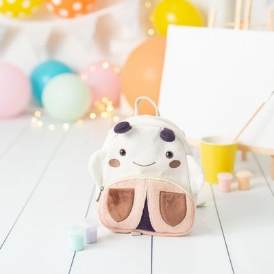 Mochila infantil branca com orelhas e bolsos castanhos em cenário colorido de festa