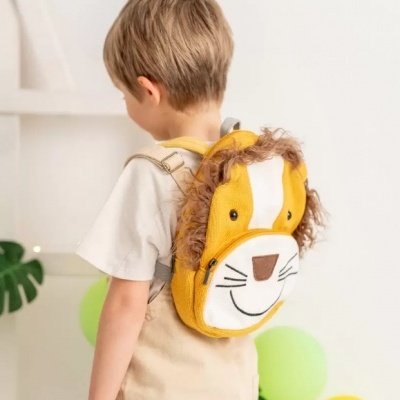 Criança com mochila de leão amarela e bege em ambiente com balões