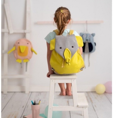 Mochila infantil elefante amarela e cinza usada por criança sentada