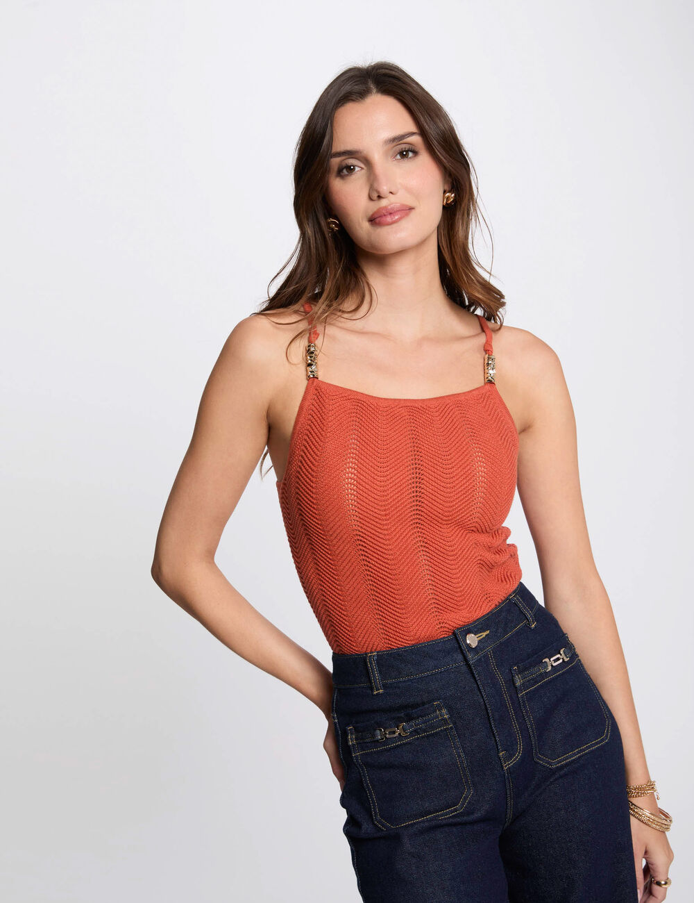 Molovic Top Top laranja de malha e calças jeans escuras num estúdio com fundo branco
