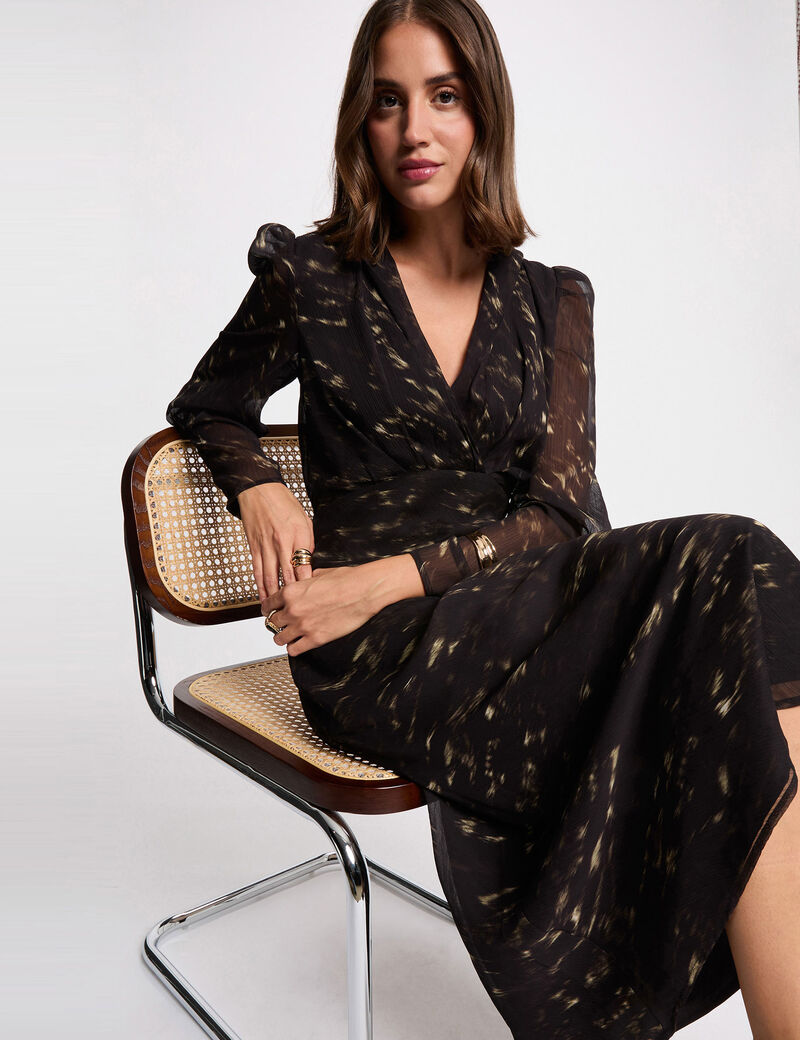 rood dress Vestido preto comprido com padrão dourado e mangas transparentes, mulher sentada numa cadeira palhinha e metal.