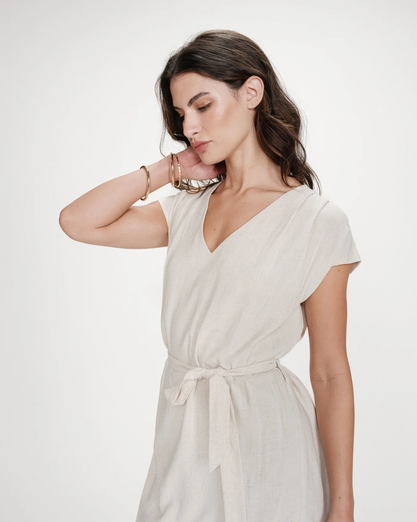marilou dress Vestido bege claro com cinto e decote em V usado por modelo com pulseiras douradas