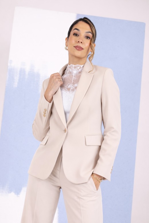 Tailored Blazer Conjunto feminino bege com blazer e calças, blusa branca de renda, fundo azul e rosa.