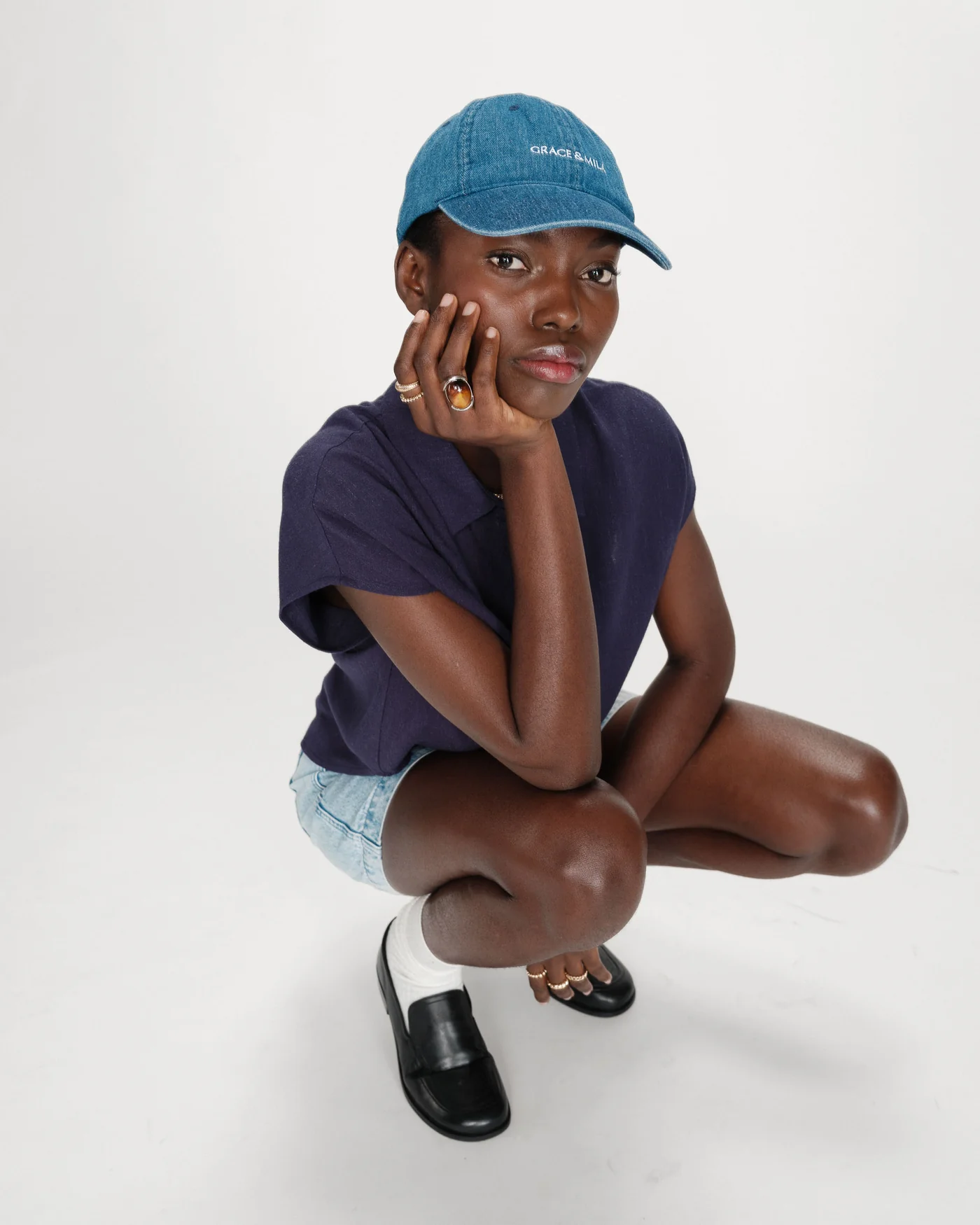 perez shirt Pessoa com boné azul, camisa roxa, calções de ganga e sapatos negros agachada sobre fundo branco