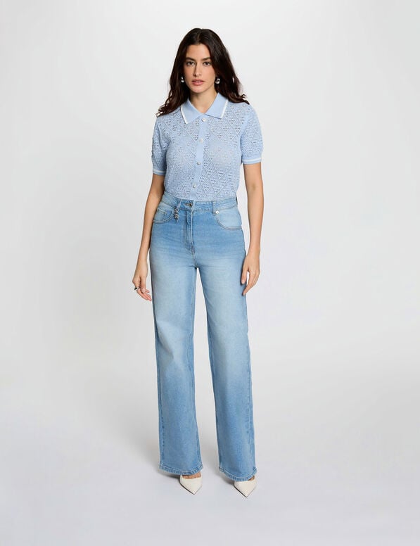 pava jeans Mulher de pé com camisola de malha azul clara, calças de ganga largas e sapatos brancos