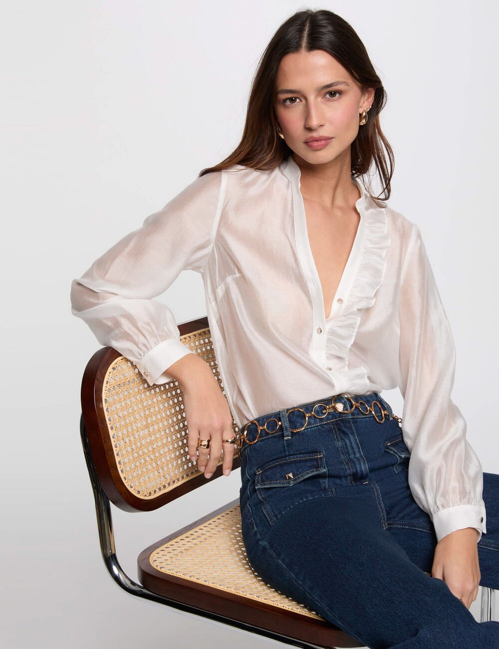 Cholie Blouse Mulher a usar blusa branca de folhos e calças de ganga azul sentado numa cadeira com assento e encosto em palhinha.