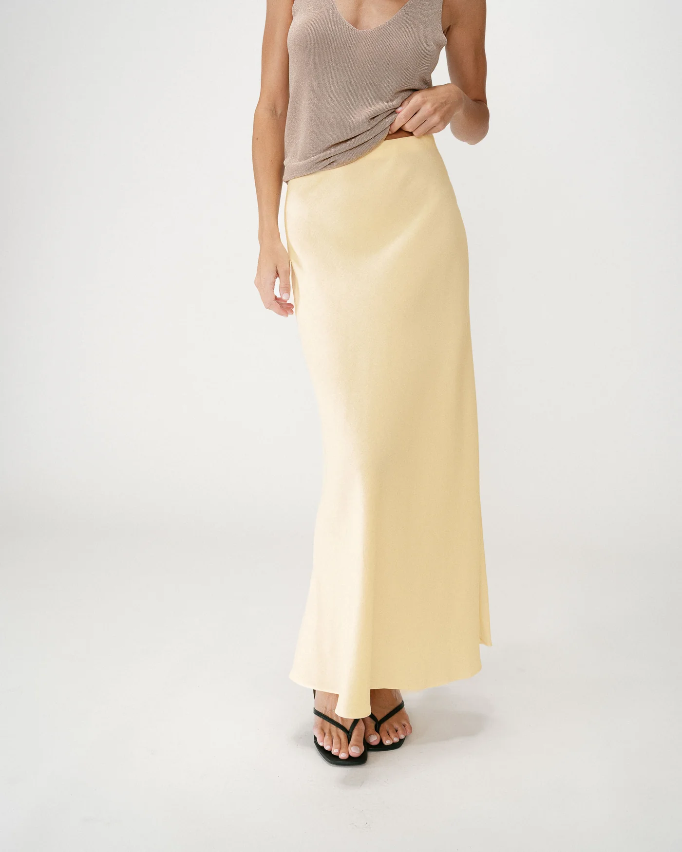 Winda Long Skirt Saia comprida amarela em cetim com top castanho claro e sandálias pretas.