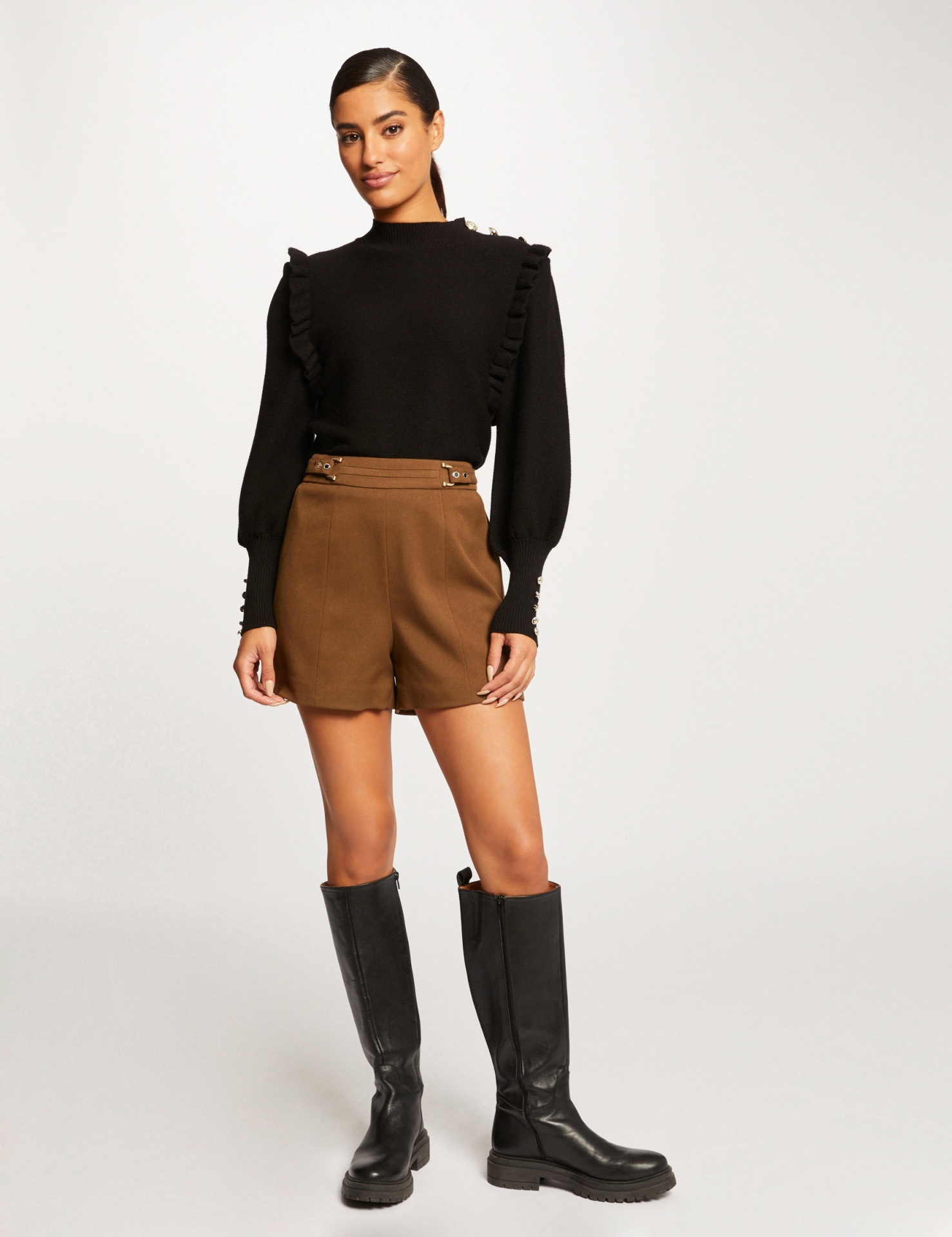 Sholky Buckle Waist Shorts Mulher a usar camisola preta com folhos e calções castanhos com botas pretas altas.