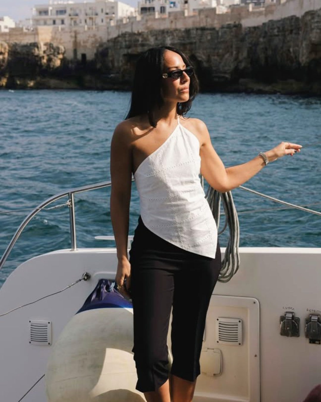 Where Capri Trousers Mulher com top branco assimétrico e calças pretas em barco no mar