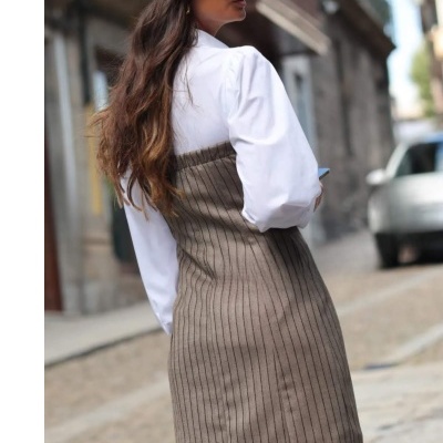 Mulher com vestido cinza às riscas e camisa branca numa rua urbana