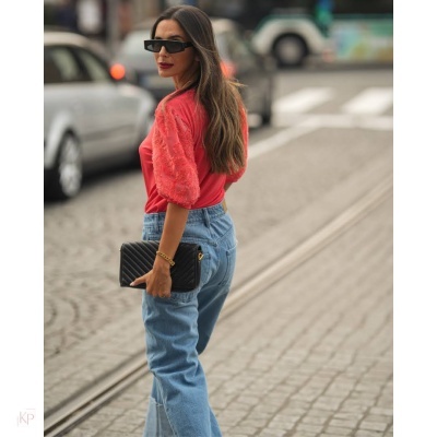 Mulher com camisola vermelha, calças de ganga e carteira preta numa rua de cidade