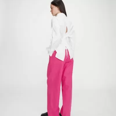 Mulher com camisa branca aberta nas costas e calças fucsia largas