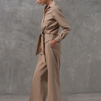 Macacão bege com cinto, calças largas e sapatos de salto baixo com padrão de oncinha em fundo cinzento.