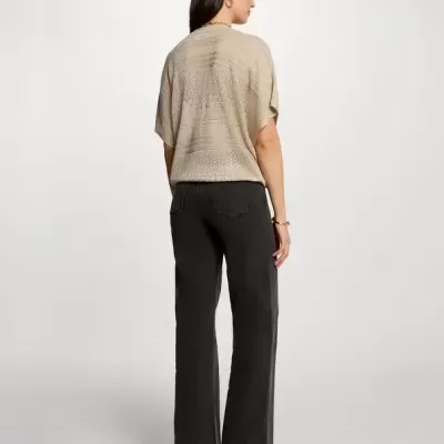 Mulher de costas com camisola bege e calças pretas em fundo branco