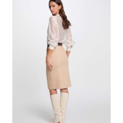 Mulher com blusa branca, saia bege e botas bege num fundo branco