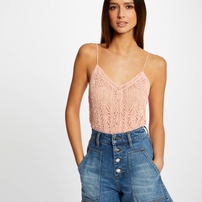 Mulher com top cor de rosa e calções de ganga azuis diante de fundo branco