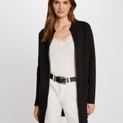 Mulher com casaco preto, top branco e calças brancas, fundo branco