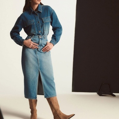 Mulher vestindo camisa de ganga, saia midi de ganga e botas de camurça castanhas.