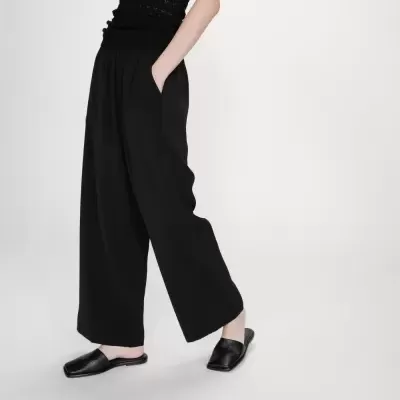 Pessoa a usar calças largas pretas, top preto de malha e sapatos pretos tipo mule com bico quadrado