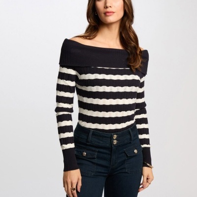 Mulher a vestir camisola de riscas pretas e brancas com gola larga nos ombros e calças de ganga azul escuro