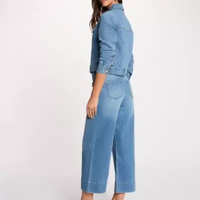Conjunto de ganga azul claro com casaco e calças largas usadas por mulher em fundo branco.