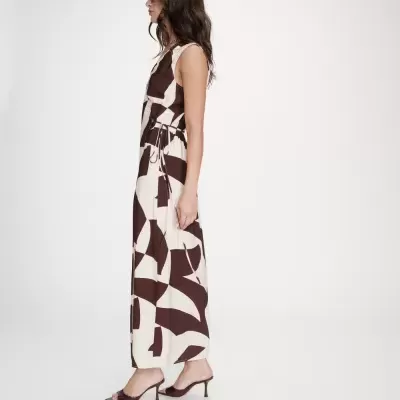 Mulher com vestido longo creme e castanho com padrão abstrato e sandálias castanhas