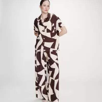 Mulher vestindo conjunto em padrão geométrico castanho e creme com camisa de manga curta e calças largas.