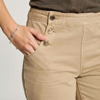 Calças de brim bege com três botões metálicos e bolso lateral esquerdo, usadas com t-shirt castanha escura