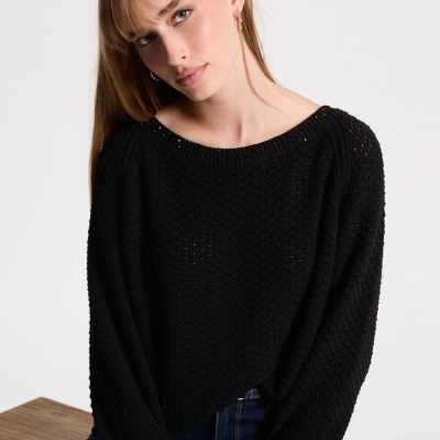 Mulher com camisola preta de malha grossa com textura de pontos e decote redondo sentada