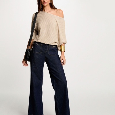 Mulher com camisola bege de malha e calças de ganga azuis largas